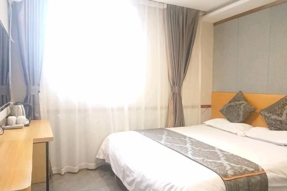 A hotel room with a bed, a desk with a kettle, and curtains.