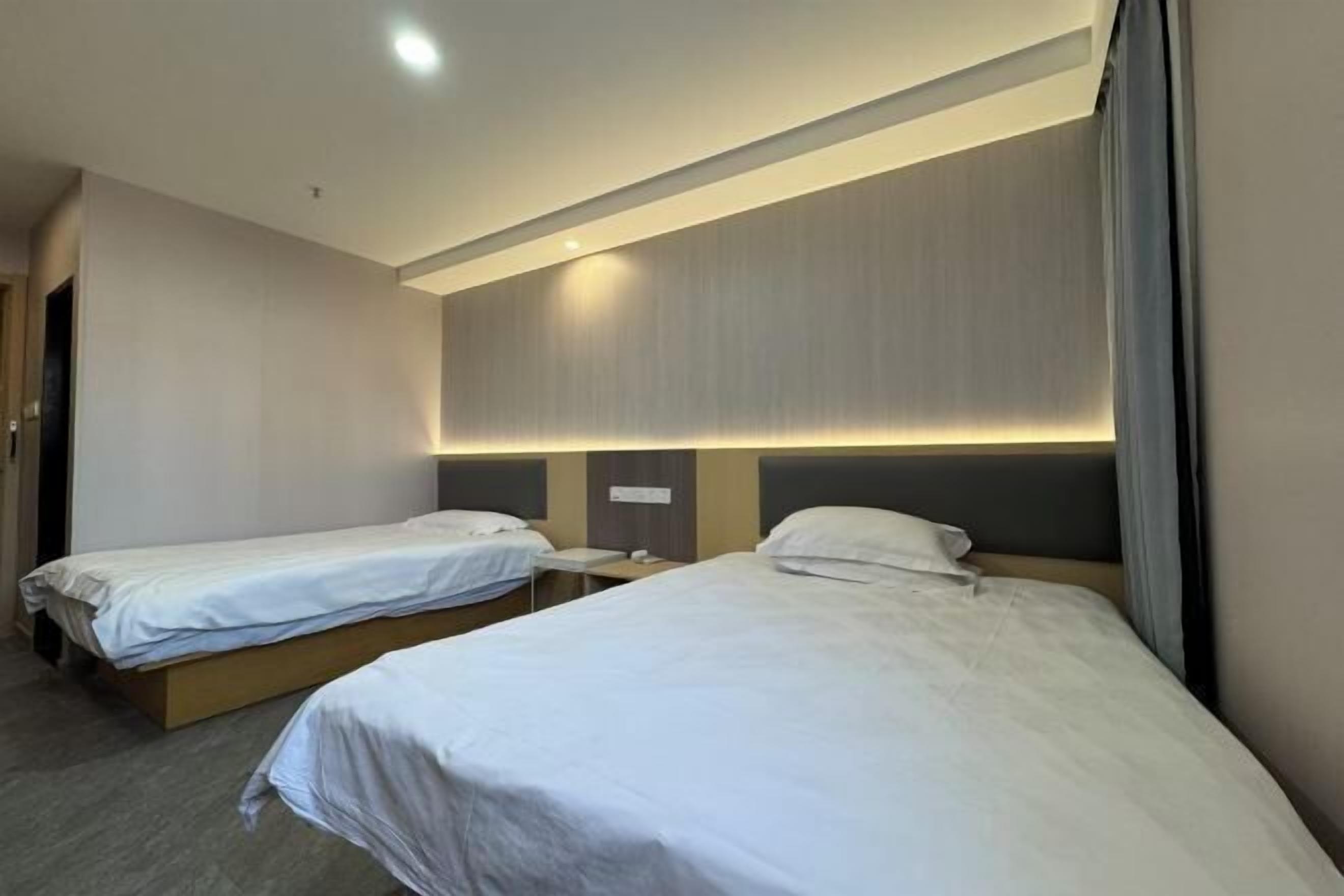 A hotel room with two single beds, a bedside table, and a headboard with built-in lighting.
