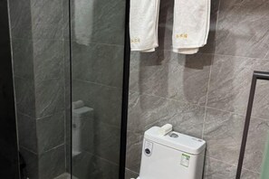A bathroom with dark marble tiles, a white toilet, and two white towels hanging on a rack. - F1 Business Hotel (Shanghai Xinhua Hospital) (Shanghai)
