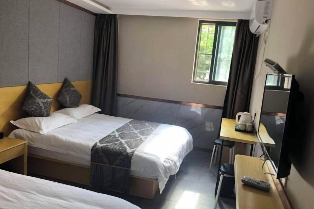 A hotel room with two beds, a desk, a chair, a TV, and a window.