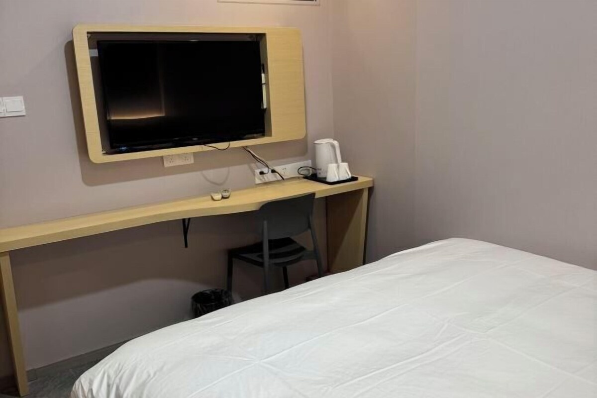 A hotel room with a bed, a desk with a television, and a coffee maker.