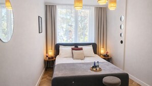 Habitación de hotel ordenada con una cama, mesitas de noche, una silla y una ventana con cortinas.