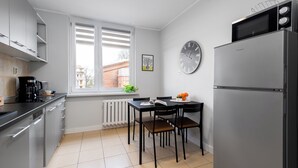 Una cocina moderna con refrigerador, microondas y cafetera. Hay una mesa de comedor con sillas y una ventana con persianas.
