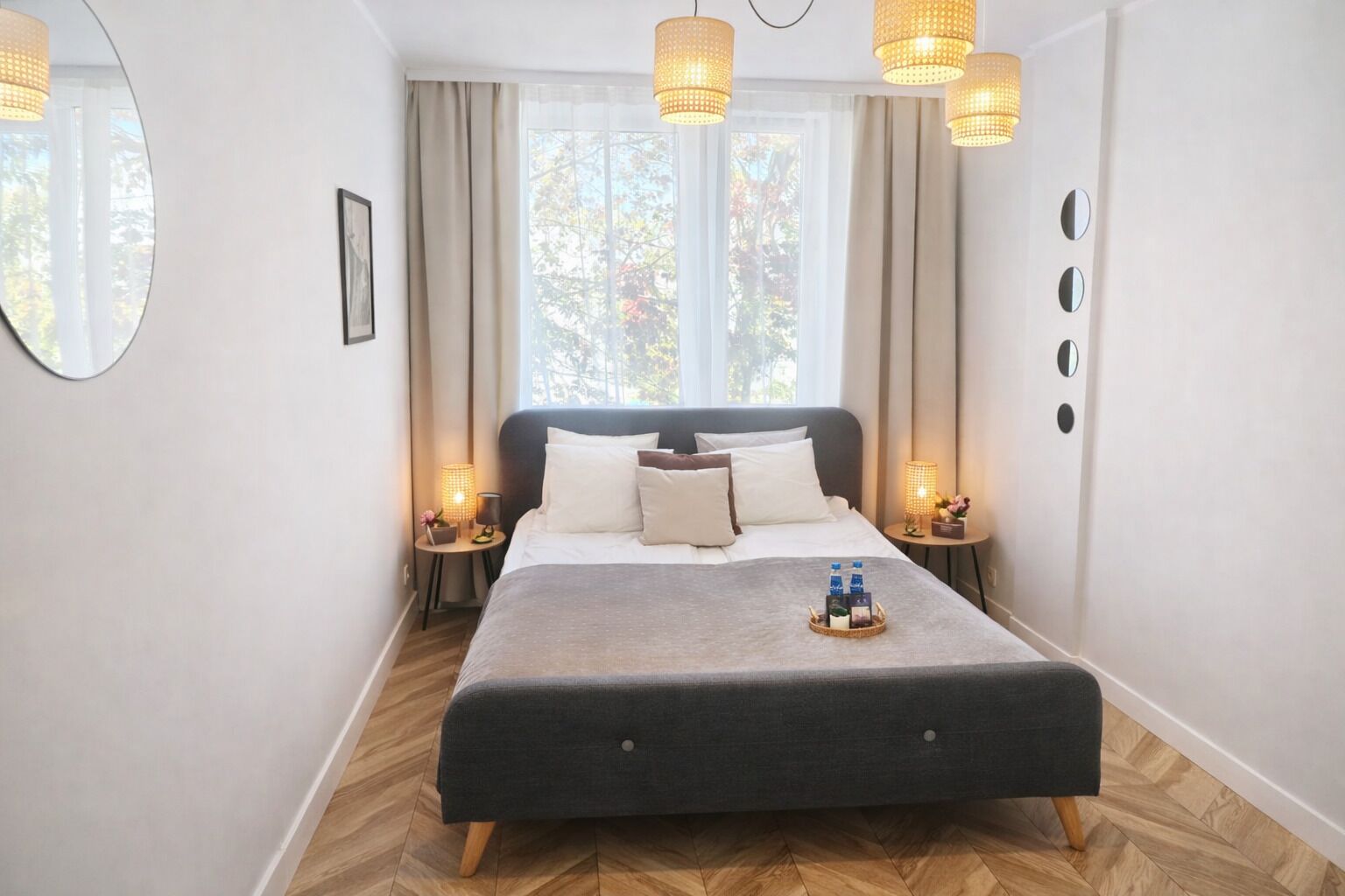 A bedroom with a bed, bedside lamps, a mirror, and a window with curtains.