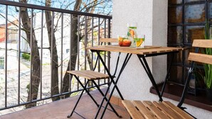 Un balcón con una mesa y sillas de madera, una planta en maceta y vistas a árboles sin hojas.