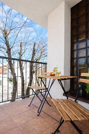 Ein Balkon mit Holztisch und -stühlen, einem Blumentopf und Blick auf kahle Bäume.