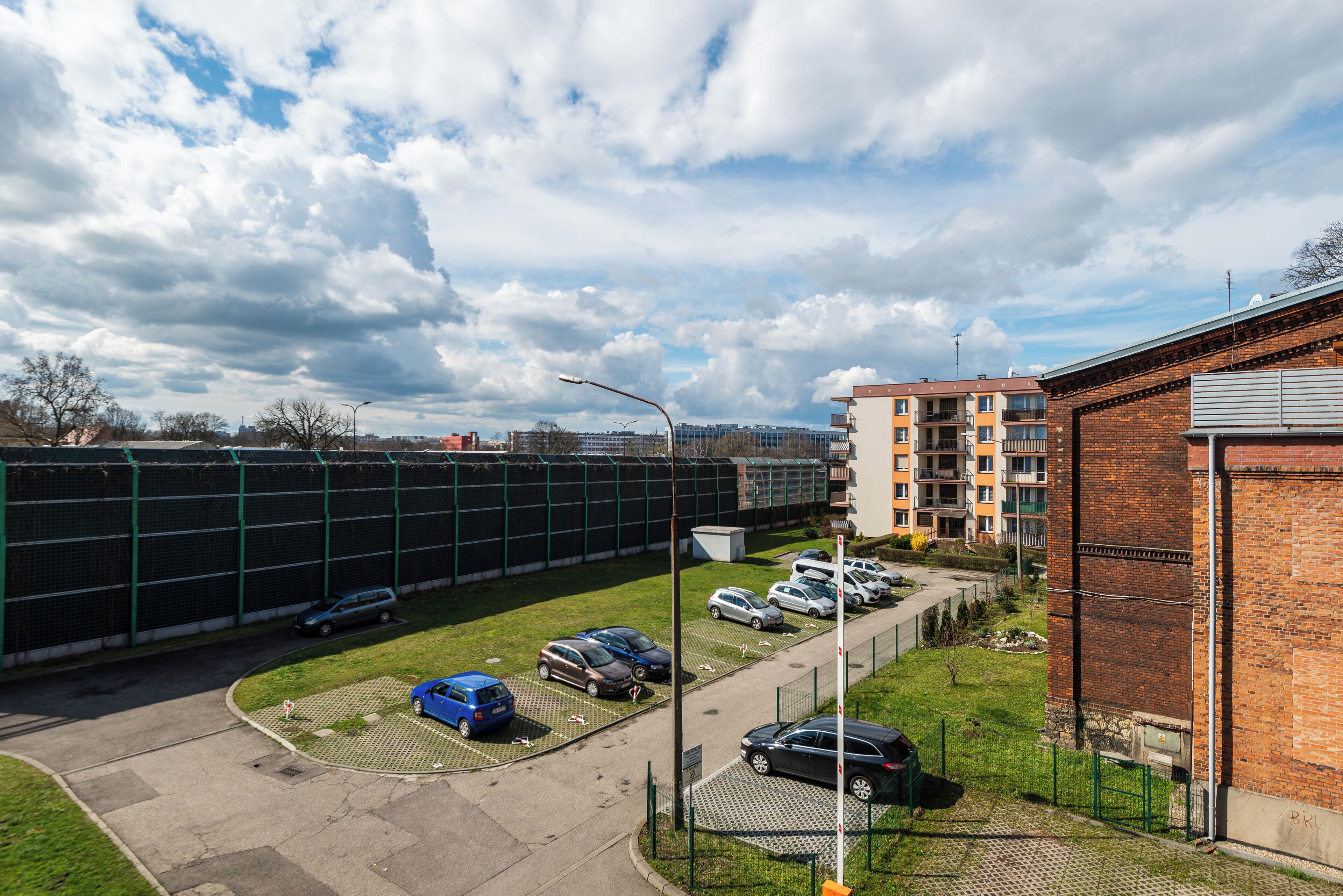 A parking lot with several cars, a grassy area, and a brick building.