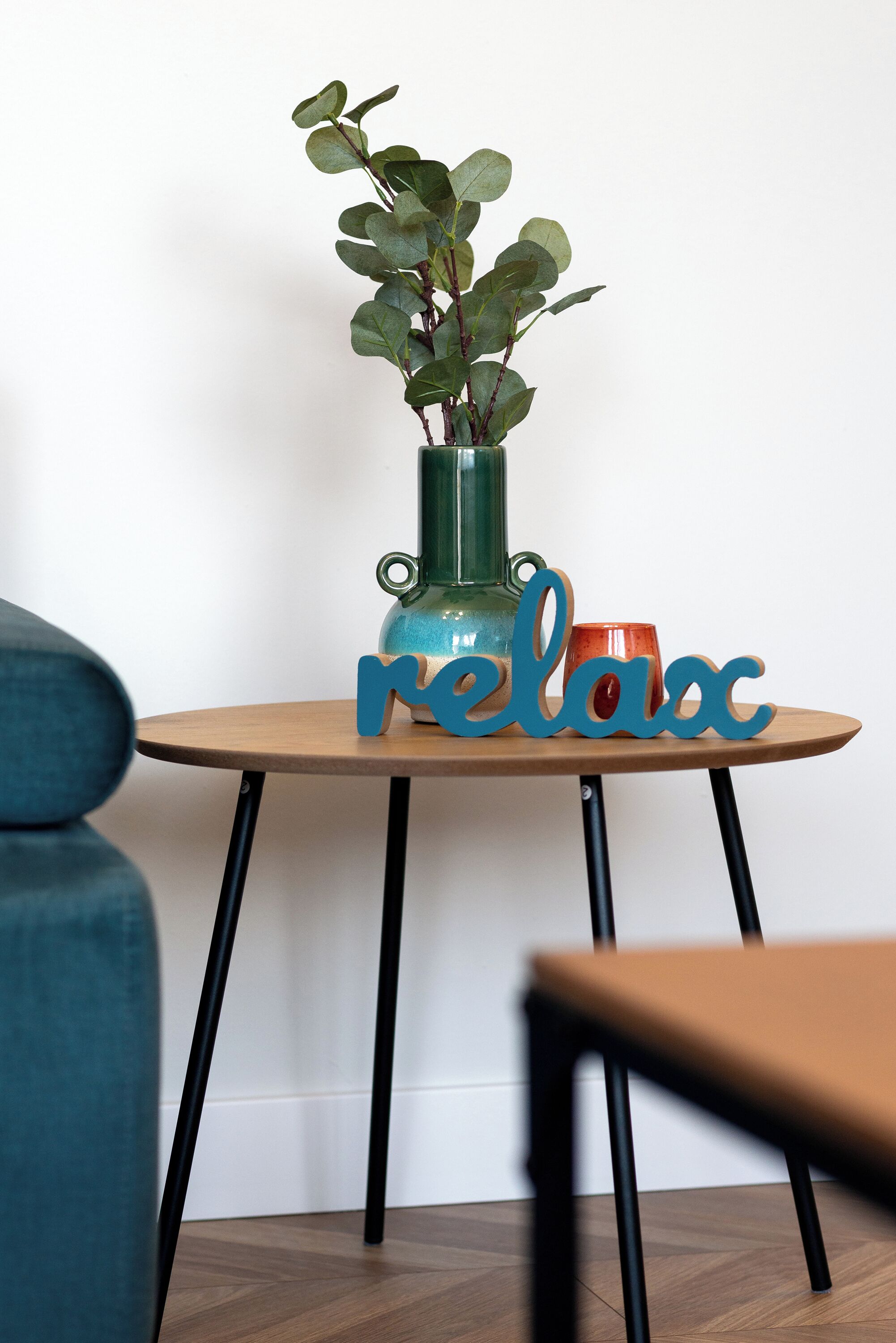 A round wooden table with a green vase and a red mug, and a blue sign that reads "relax".