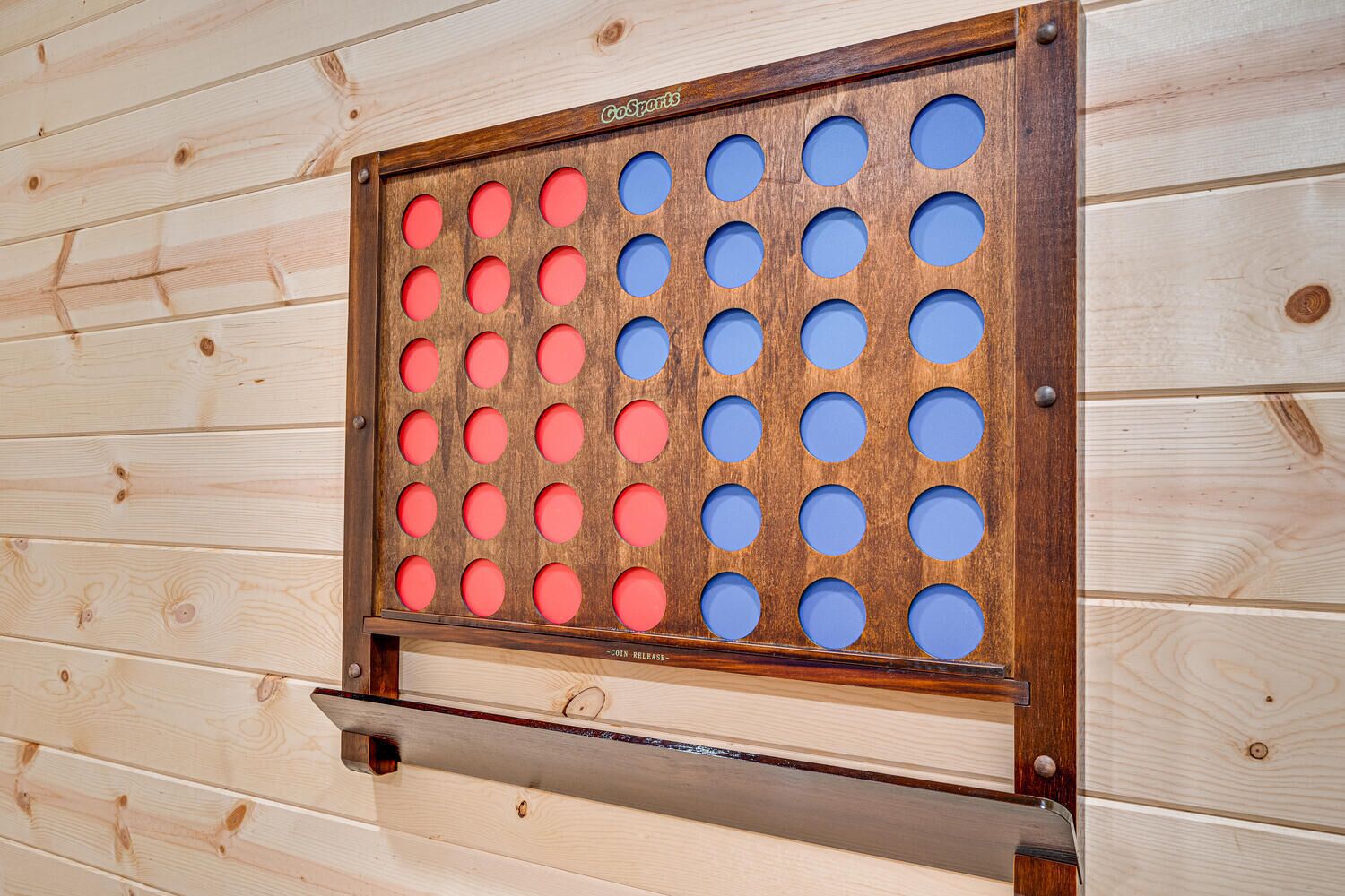 A wooden board with circular holes, some red and some blue, mounted on a wooden wall.
