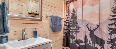 A wooden cabin bathroom with a sink, mirror, and shower curtain featuring a deer and forest design.