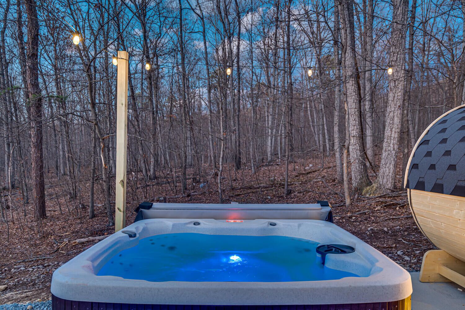 A hot tub in a forested area with string lights.