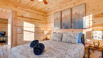 A wooden cabin bedroom with a bed, a ceiling fan, and three paintings on the wall.