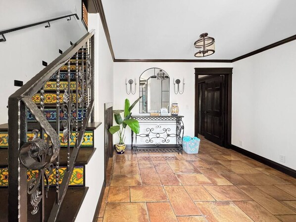 Uma escadaria com grades de metal elaboradas, um aparador com objetos decorativos e um vaso de planta.