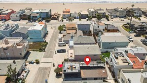 An aerial view of a coastal residential area with a variety of houses, a beach in the background, and a red location marker indicating a specific building.