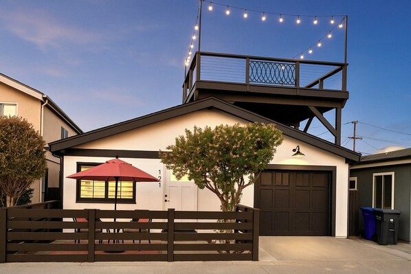 A modern house with a garage, a tree in front, and string lights on the roof. - 360 Ocean View Roof Deck, 50 Steps to Beach+AC! (Oxnard)