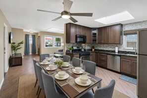 A modern kitchen with dark wood cabinets, stainless steel appliances, and a dining area set for four with a table set for a meal. - 360 Ocean View Roof Deck, 50 Steps to Beach+AC (Oxnard)