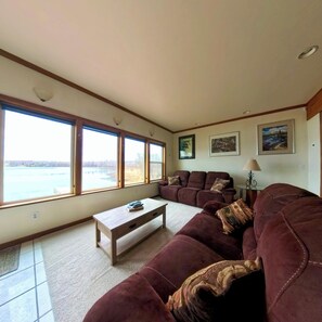 A living room with a large window, a sofa, a coffee table, and wall art. - Downtown Wasilla Lakefront Home w/private dock (Wasilla)