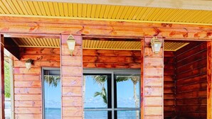 A wooden building with large glass doors and windows, a covered entrance, and a view of the beach. - Miti Maninoa Ocean Club (Maninoa)