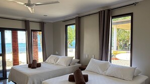 A hotel room with two beds, a ceiling fan, and large windows offering a view of the beach. - Miti Maninoa Ocean Club (Maninoa)