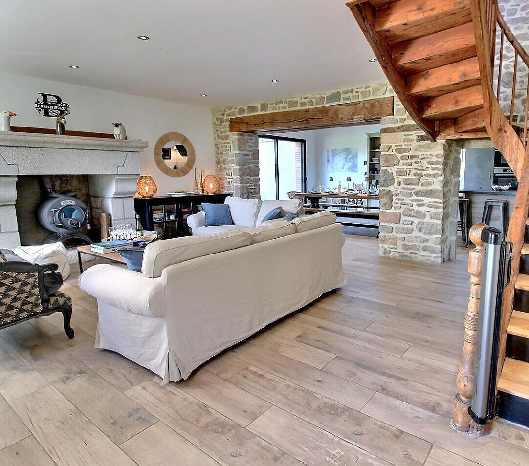A spacious living room with a stone fireplace, a sofa, and a wooden staircase.