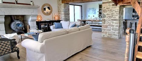 A spacious living room with a stone fireplace, a sofa, and a wooden staircase.
