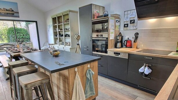 A modern kitchen with a central island, bar stools, a built-in oven, and a coffee machine.