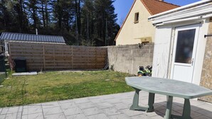 A patio area with a green table, a wooden fence, and a building with a tiled roof.