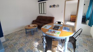 A dining area with a round table, chairs, a small side table, a brown sofa, and a patterned floor.