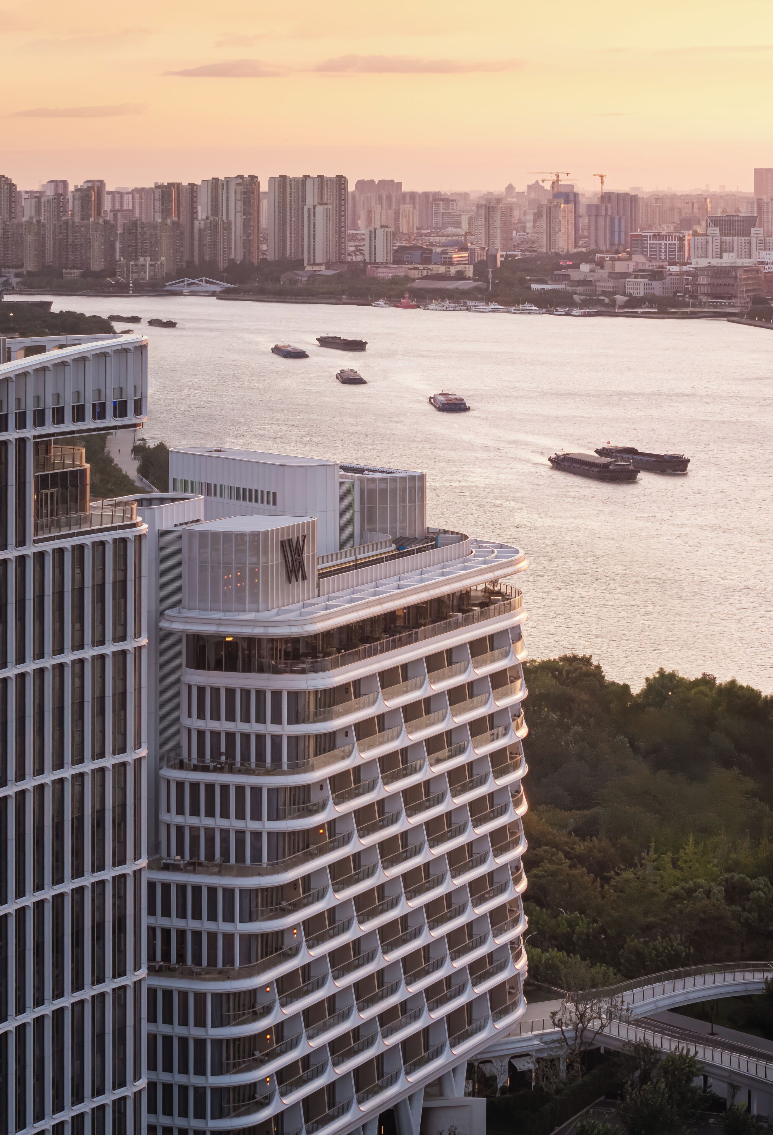 A high-rise hotel with multiple balconies and a view of the river with boats.