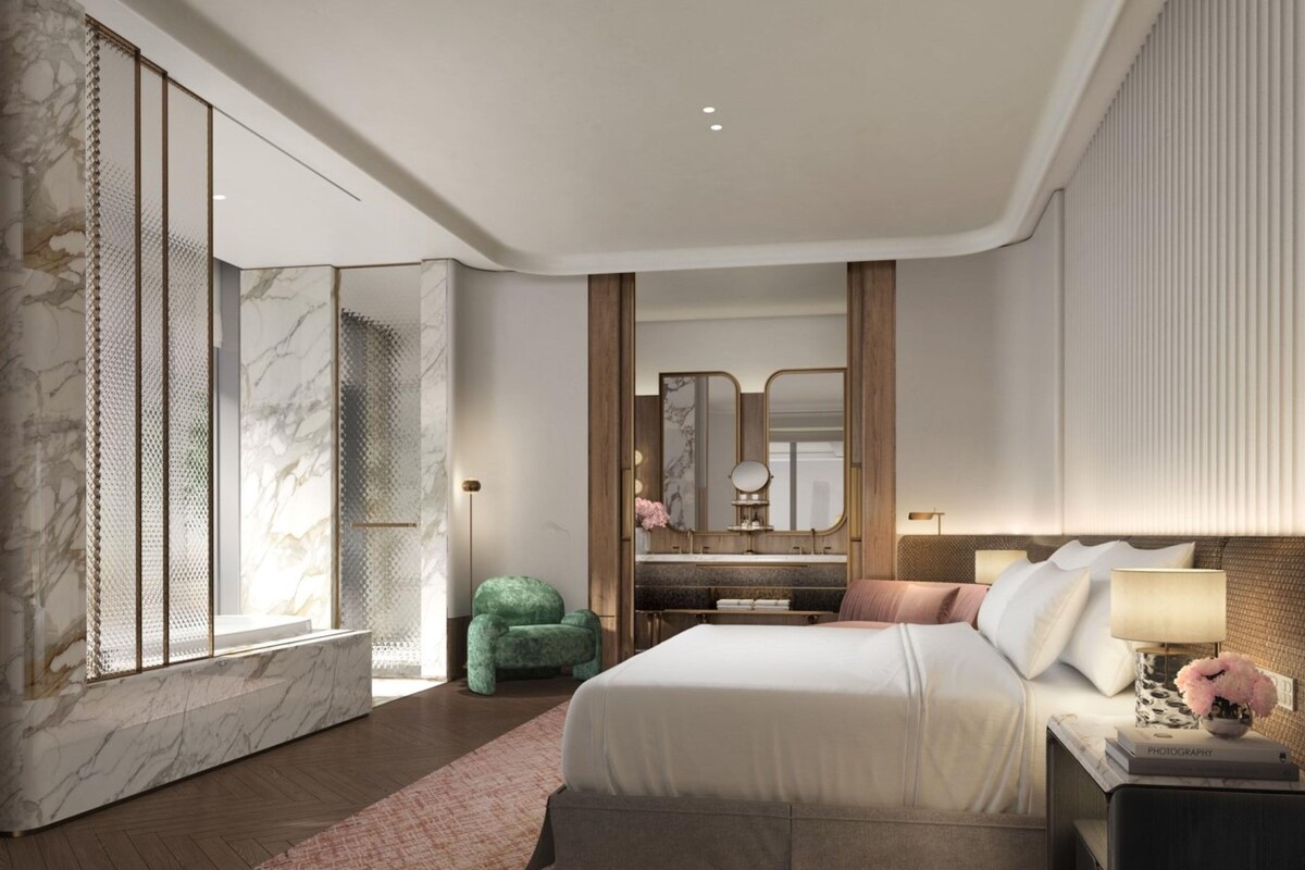 A modern hotel room with a marble accent wall, a large bed with a headboard, a bedside table with a lamp, and a mirror.