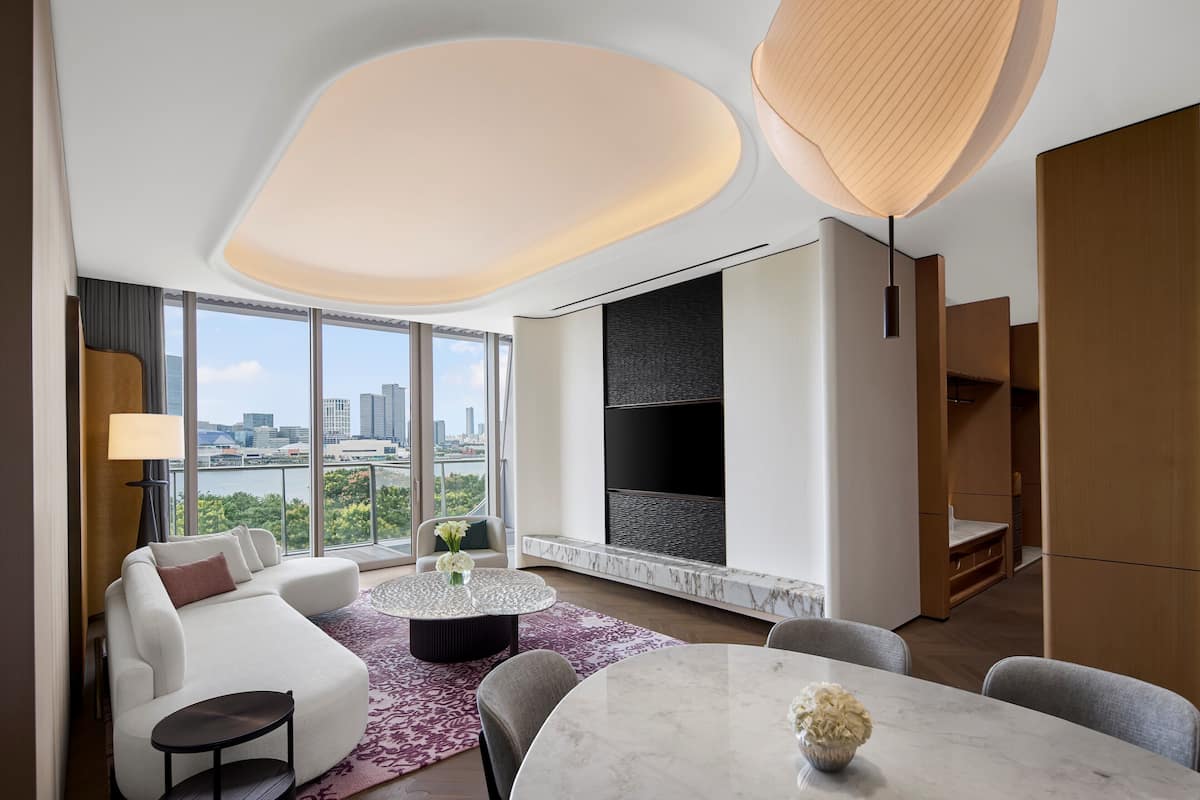 Ein modernes Hotelzimmer mit großem Fenster und Blick auf die Stadt, einer Sitzecke, einem Esstisch und einem Flachbildfernseher.