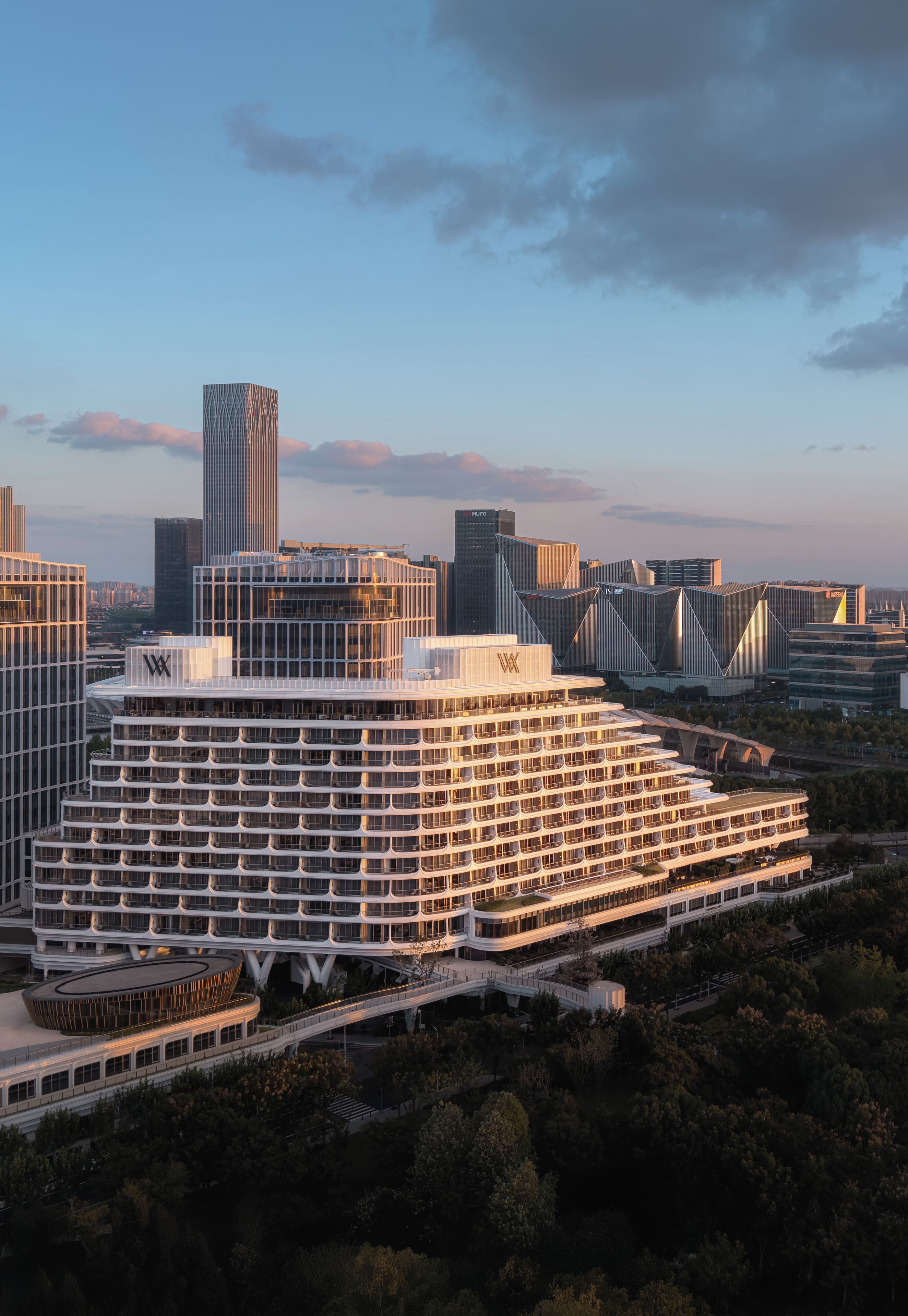A modern hotel with a unique layered design, surrounded by other high-rise buildings and trees.