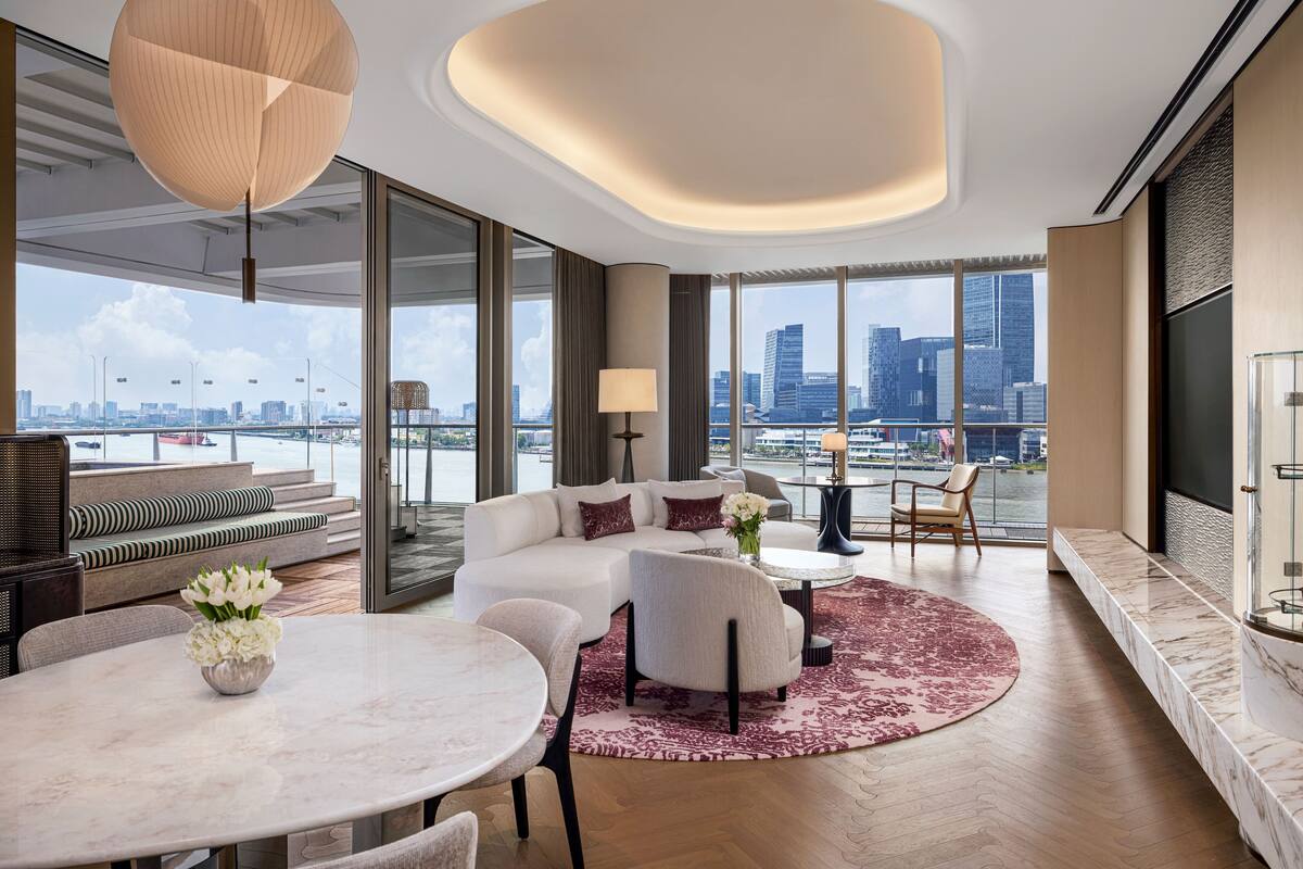 Ein modernes Wohnzimmer mit einer Couch, Sesseln, einem Esstisch und einem großen Fenster mit Blick auf die Stadt.