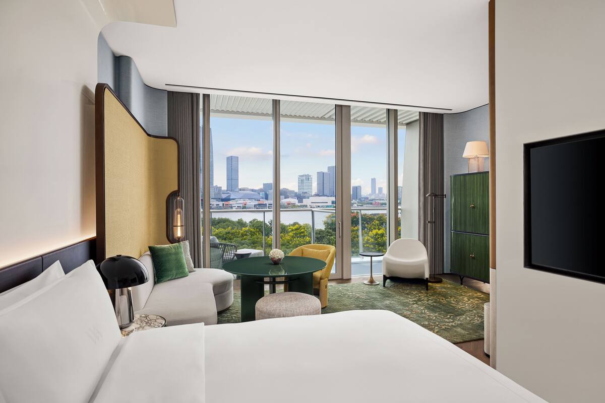Ein Hotelzimmer mit einem großen Bett, einer Sitzecke mit Tisch, einem Fernseher und Blick auf die Stadtlandschaft.