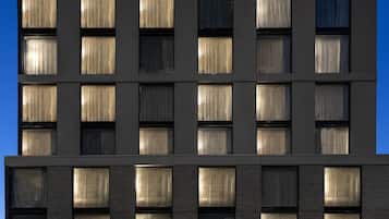 Un moderno edificio de hotel con varios pisos, amplias ventanas con cortinas y una entrada visible con señalización.