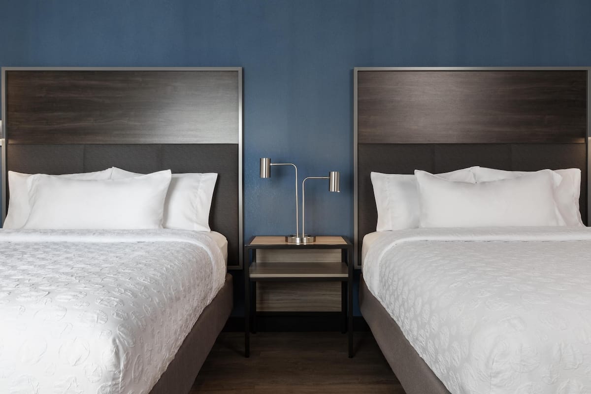 Habitación de hotel con dos camas, una mesita de noche entre ellas y una lámpara moderna.
