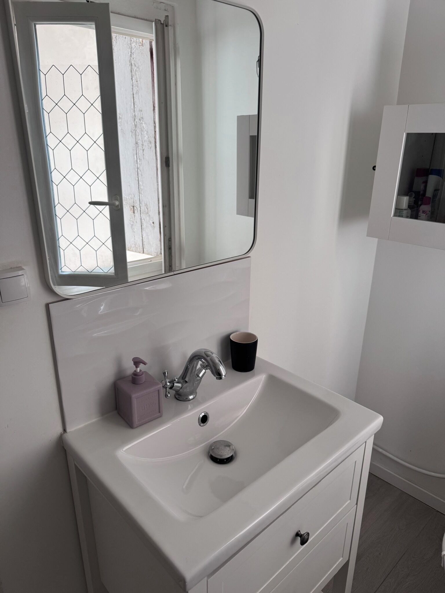 Un bagno con un lavandino bianco, uno specchio e una finestra con motivo esagonale.