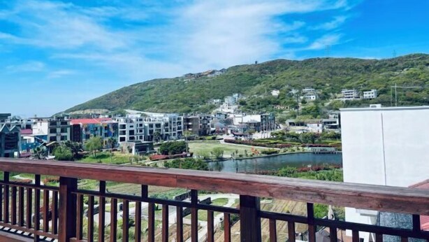 A view of a residential area with modern buildings, a lake, and a hill in the background. - Donghai Fishing Village Ganhai Renjia Guest House (Shengsi)