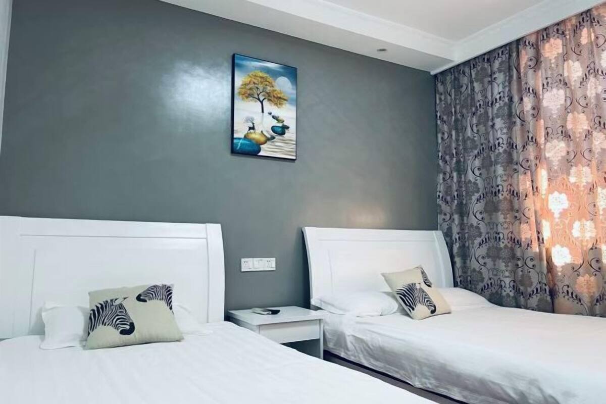 Ein Hotelzimmer mit zwei Betten, einem Nachttisch, einem Gemälde und einem Vorhang.