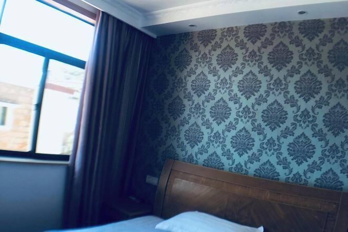 Ein Zimmer mit Bett, einem fensterbelaubten Fenster und Wandtapete mit Muster.