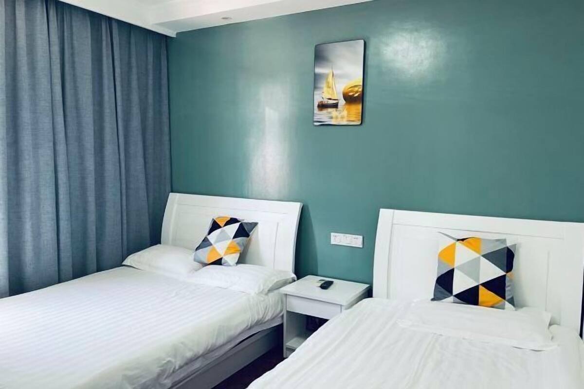 Ein Hotelzimmer mit zwei Betten, einem Nachttisch, einem Bild an der Wand und einem Fenster mit Vorhängen.