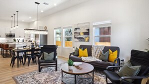 A modern living room with a sofa, chairs, a coffee table, and a dining area with chairs and a table. - Sleek 4BR 3BA Urban Living w Downtown Views (San Antonio)