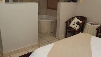Habitación de hotel con cama, una silla, una mesita, televisor y baño.