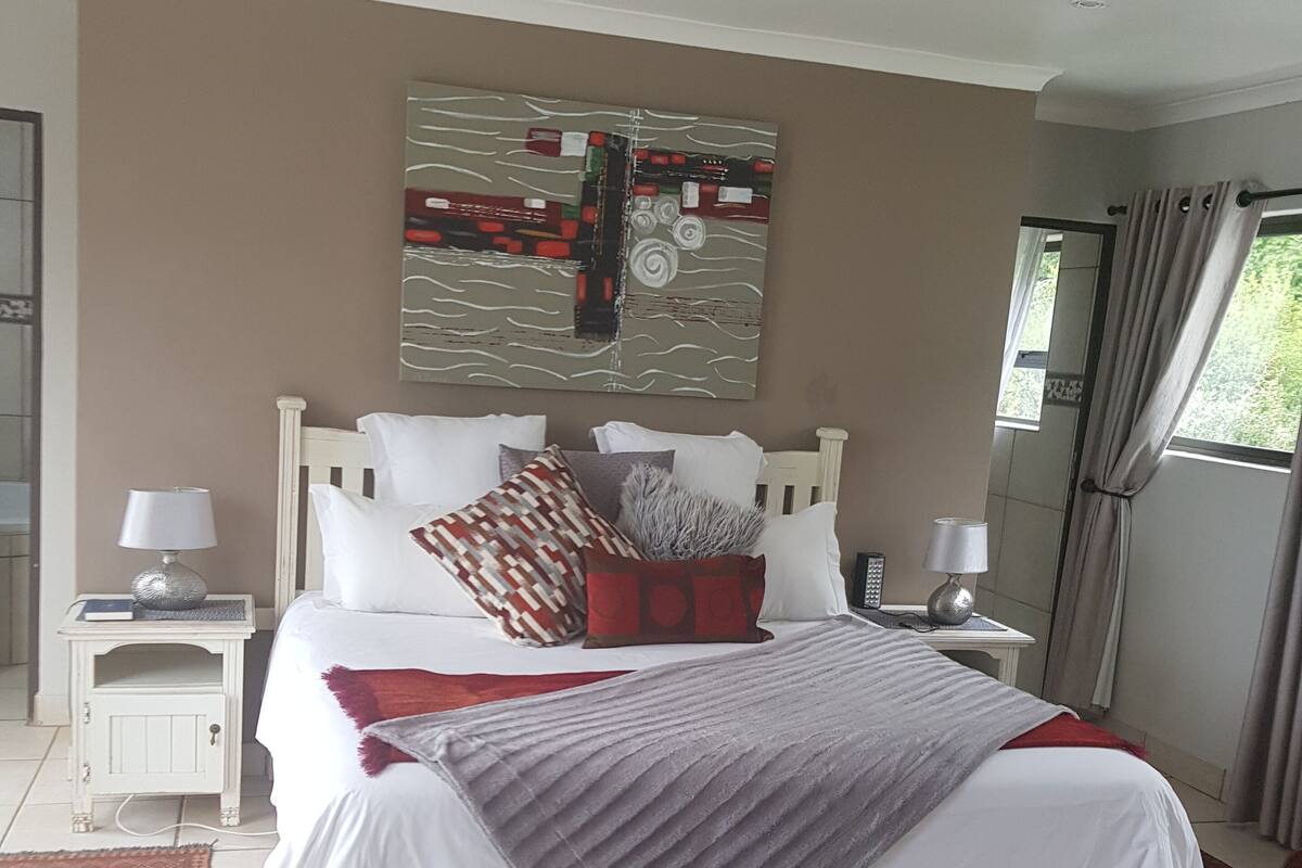 Quarto com uma cama grande, duas mesas de cabeceira, um criado-mudo, uma cadeira e uma janela com cortinas.