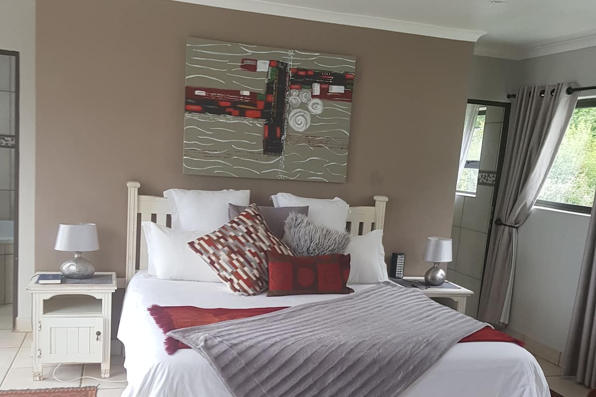 A bedroom with a large bed, two bedside tables, a nightstand, a chair, and a window with curtains.