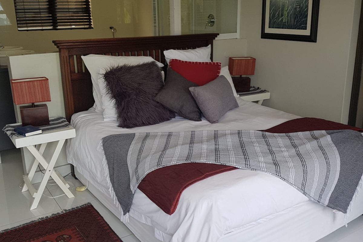Quarto com cama, mesa de cabeceira, espelho, janela com persianas e ar condicionado fixado na parede.
