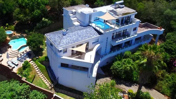 A modern multi-story house with a rooftop pool, surrounded by lush greenery. - El Shadai Guest House  Hartbeespoort (Hartbeespoort)