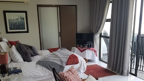 A spacious bedroom with a large bed, a TV, and a balcony with curtains. - El Shadai Guest House  Hartbeespoort (Hartbeespoort)