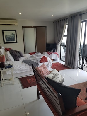 A spacious bedroom with a large bed, a TV, and a balcony with curtains.