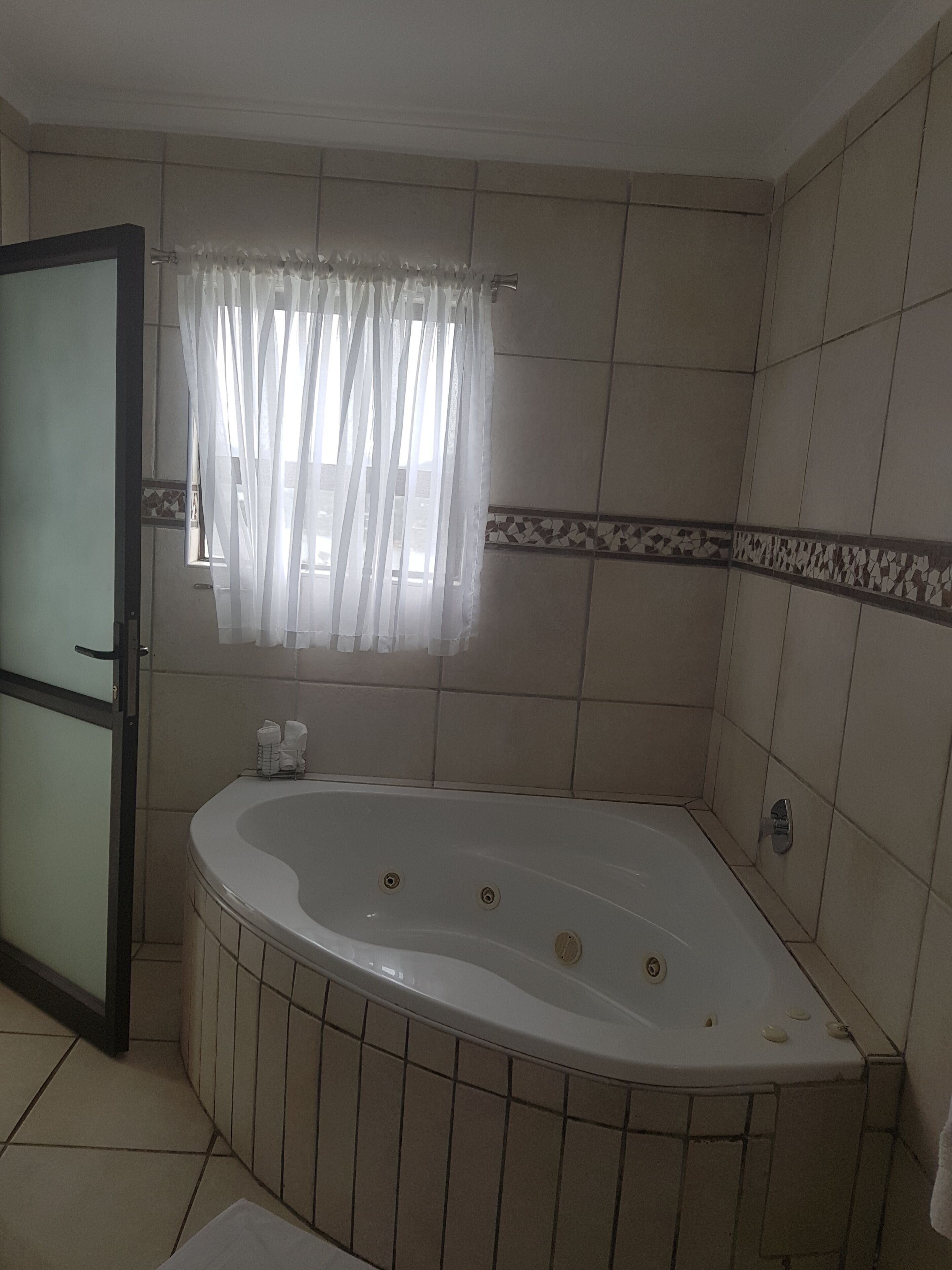 A bathroom with a bathtub, a shower, and a window with curtains.